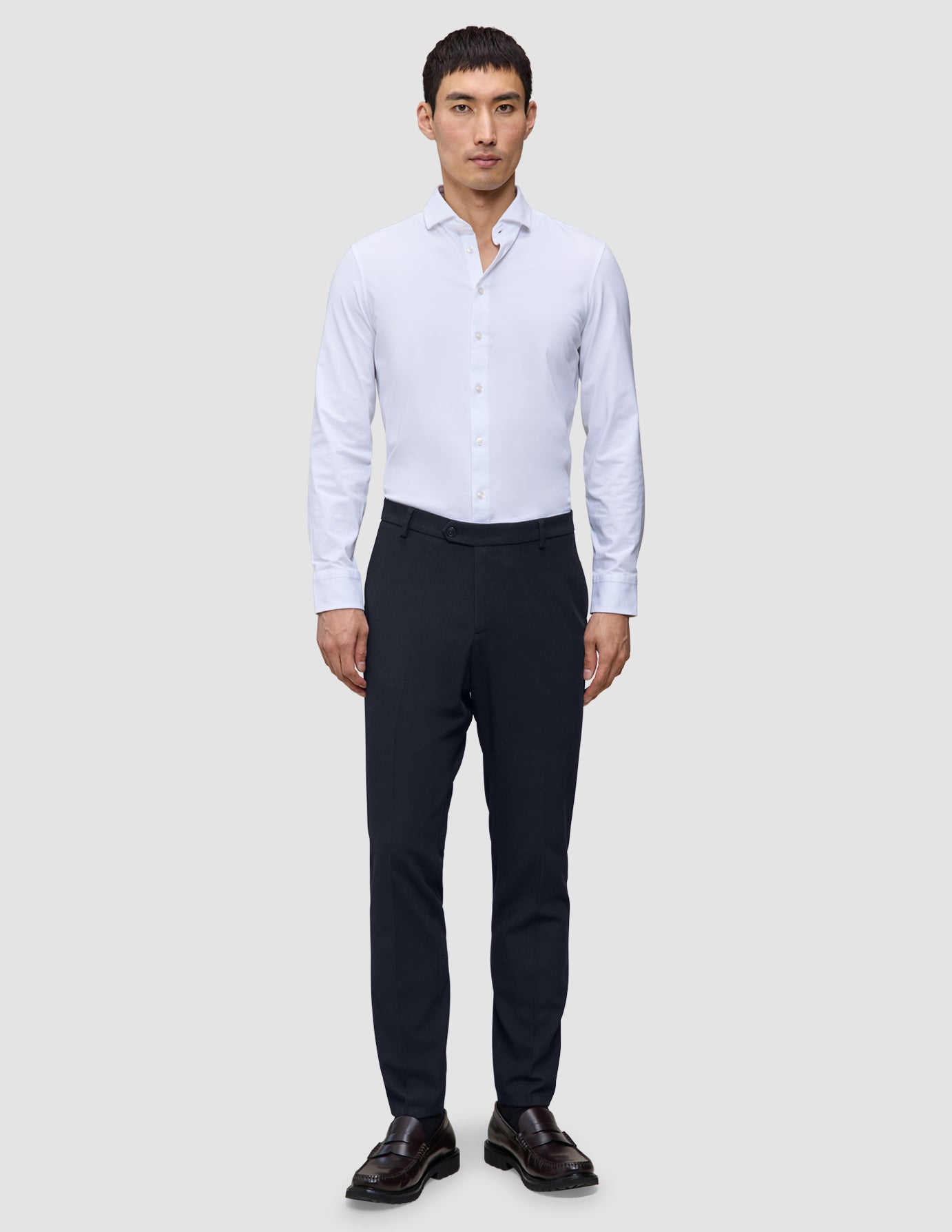En mand iført en hvid skjorte med knapper, Motion Suit-bukser i slim fit i midnatsblå og mørkebrune loafers.